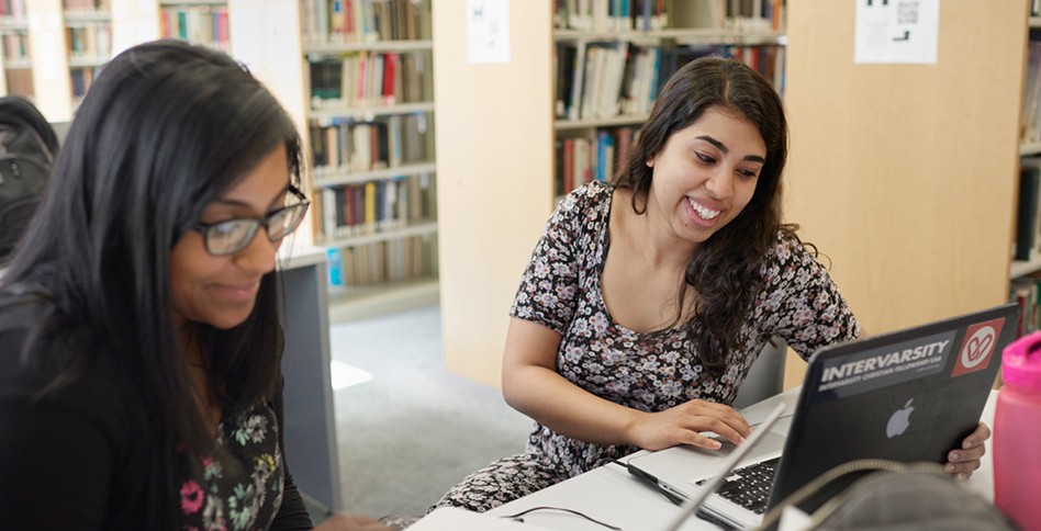 Two students looking at laptops in library