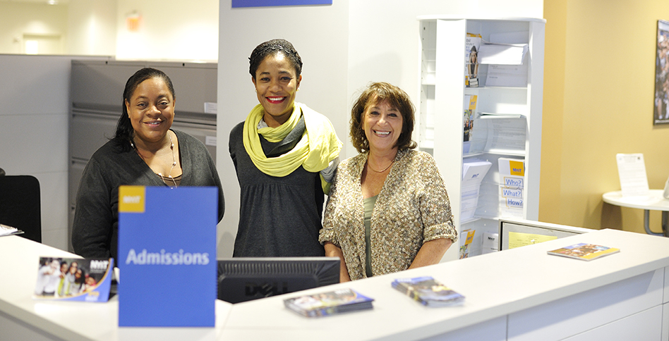 Three admissions personnel smiling behind check-in desk