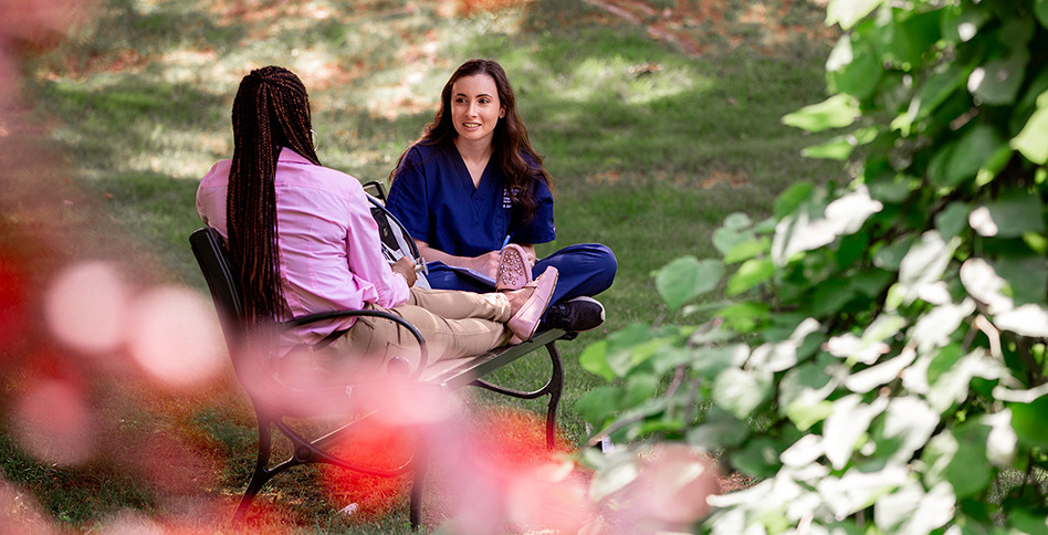 Two female students talking outside on bench