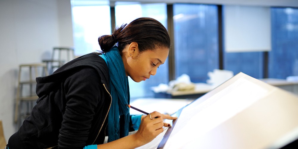 Woman draws on drafting table.